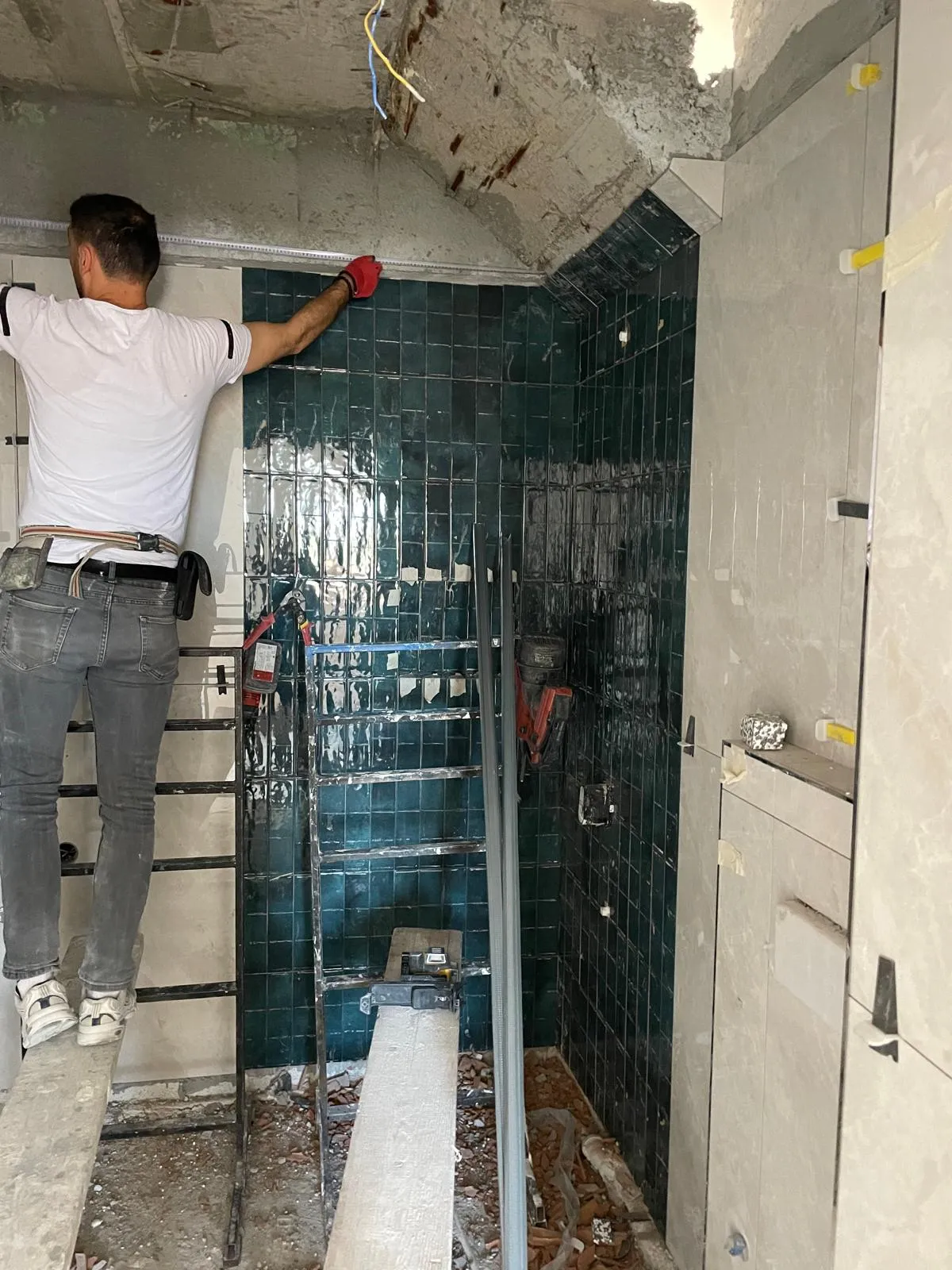 Duş alanında koyu yeşil seramik kaplama uygulaması yapan usta