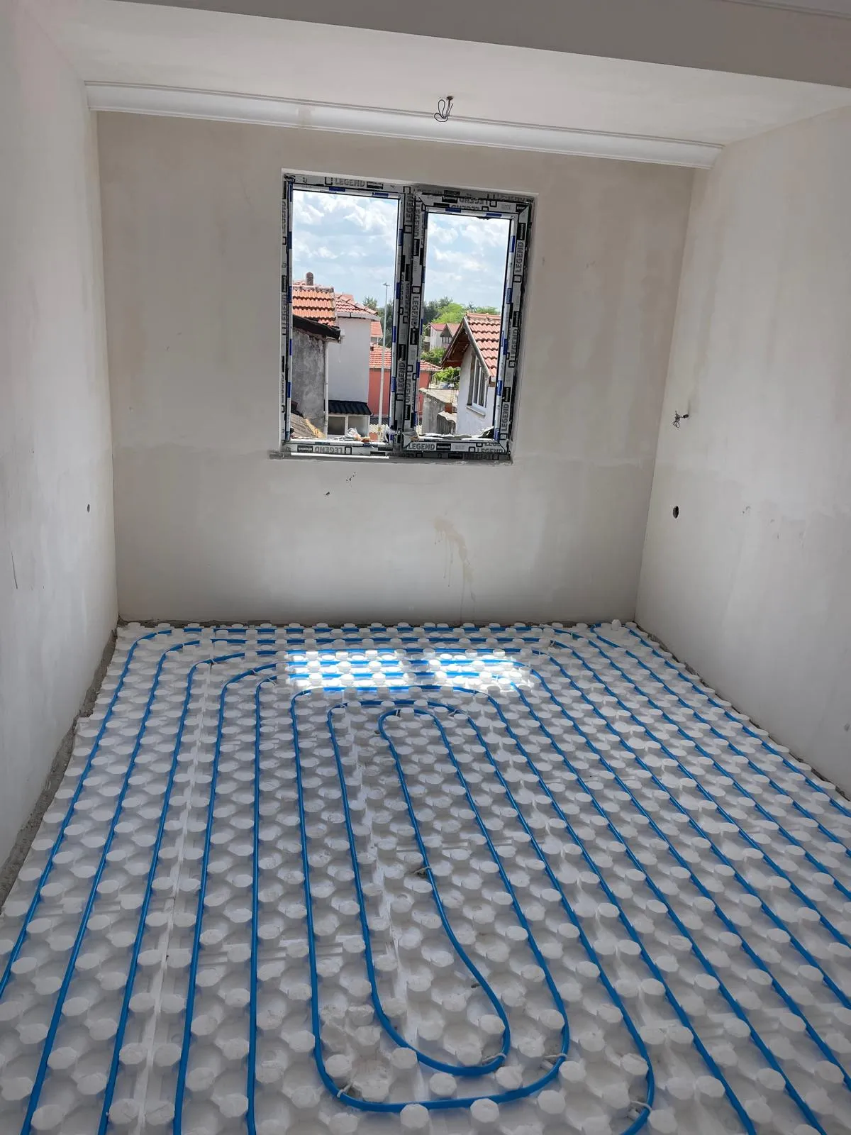 Pencereli bir odada döşenmiş yerden ısıtma boruları